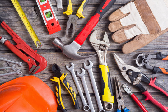 A collection of essential hardware tools spread across a wooden workbench, including a claw hammer with a wooden handle,