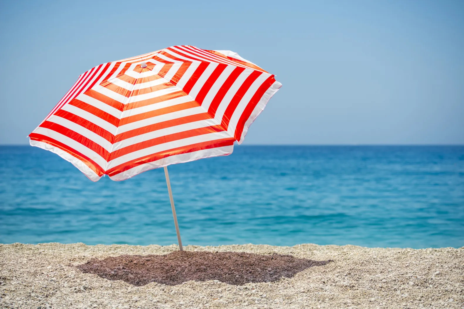 "A colorful beach umbrella with a wide, striped canopy providing shade, anchored securely in the sand with a sturdy metal frame, set up on a sunny beach.