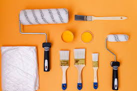 A variety of paint brushes and paint rollers displayed on a clean surface, including different brush sizes and shapes for detailed work, and smooth rollers with high-density covers for even paint application.